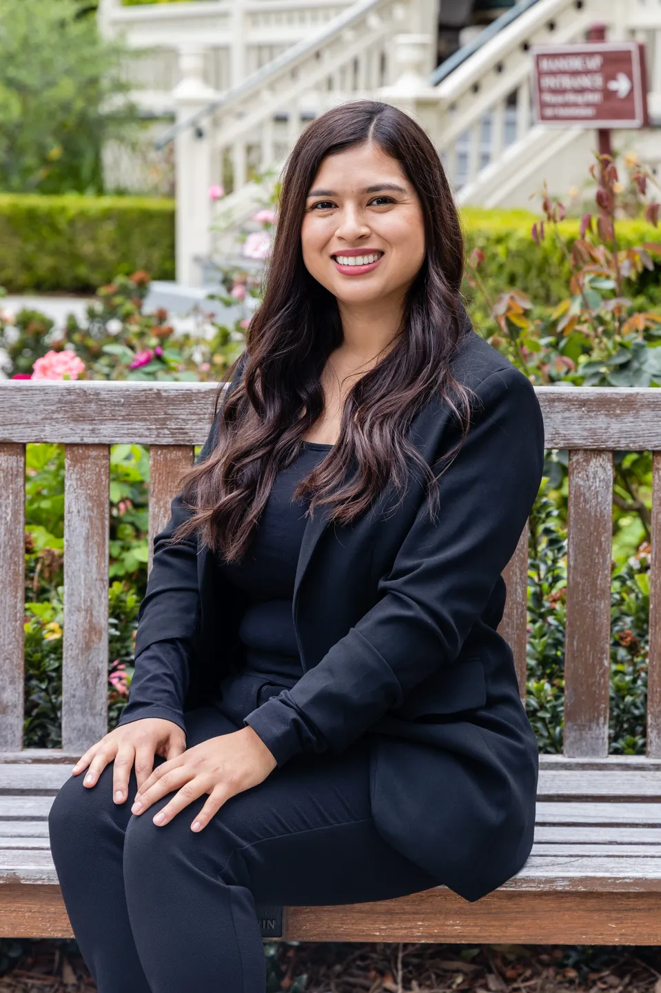 Woman in black suit sitting on a bench smiling.