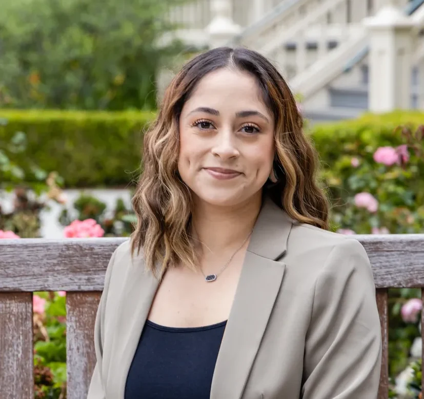 Professional woman with long hair smiling outdoors on a bench.