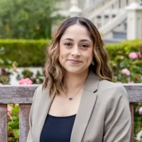 Professional woman with long hair smiling outdoors on a bench.