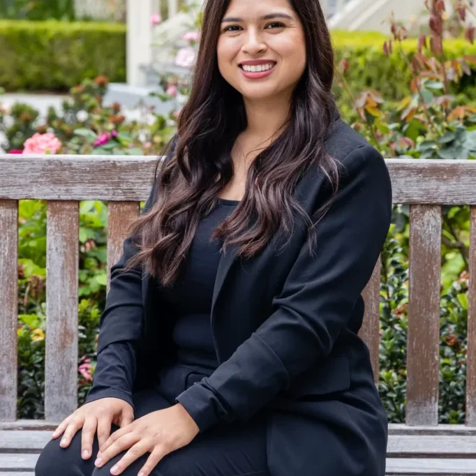 Woman in black suit sitting on a bench smiling.